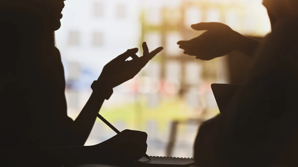 Fluency Edge - Neurolanguage Coach für Englisch und Deutsch - Silhouette eines jungen Designerteams, das mit Laptop und Notebook in der Hand steht und über das neue Projekt diskutiert/spricht
